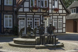 Sculptures at a fountain in front of a traditional half-timbered house in a quiet city street,