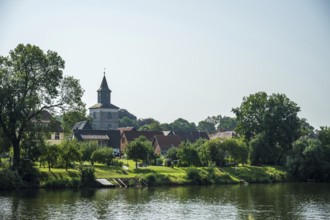 Village by the river with church and lush greenery, relaxed rural atmosphere under a clear sky,