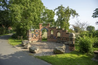Brick wall with archway in a sunny park next to a path and trees, Bücken, district of Nienburg