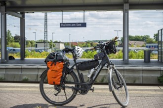 A bicycle with panniers stands at Haltern am See station, surrounded by summery nature and railway