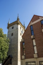 Historic tower and modern building, surrounded by trees, under a blue sky, tower of the old St