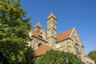 Gothic church with red tiled roofs, surrounded by green trees under a blue sky, St. Mary's Church