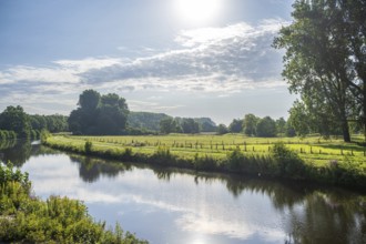 Sunny day by a river, green meadow and trees in the distance under a bright sky, Ems near