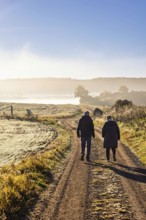 Two people walking on gravel road in the countryside a misty autumn morning, Sweden