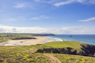 Sunny seascape view in a coastal landscape with a sandy beach and a rocky coastline from a meadow,