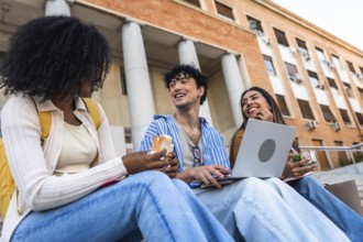 Group of happy young multiracial students sitting on steps outside a university building, enjoying