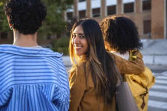 Diverse young adult students walking on a university campus during the day, one female student