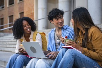 Group of multi ethnic university students sitting on outdoor steps, sharing a light meal, laughing,