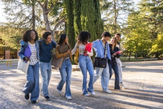 Group of young diverse students walking arm in arm, smiling and chatting while carrying books and