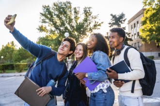 Diverse group of smiling university students recording a selfie outdoors on campus, holding books