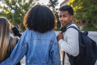 Three diverse young university students walking together on campus, the smiling man looking back at