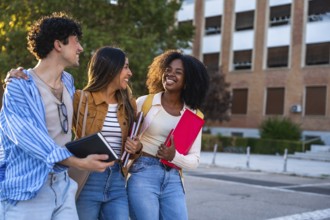 Group of diverse university students walking together on campus, smiling, holding notebooks and