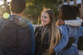Group of young diverse university students walking arm in arm on campus, one woman turning to
