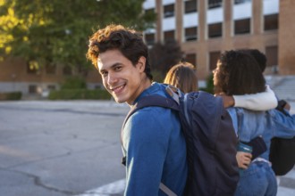 University student smiling at the camera with a backpack, walking with friends on campus, showing