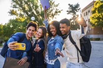 Diverse group of happy young students smiling and waving while taking a selfie together at a