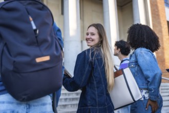Students walking on campus, young woman smiling and looking back as friends chat and head to class,