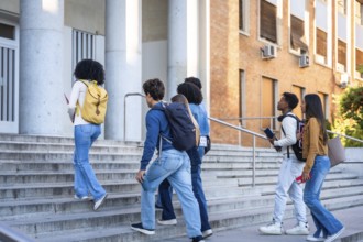 Group of multi ethnic students with backpacks and books walking up the steps of a university