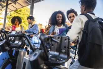 Young diverse students are talking and smiling at a public bicycle sharing station, using