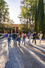 Group of diverse university students hurrying with textbooks and backpacks on a cobblestone path,