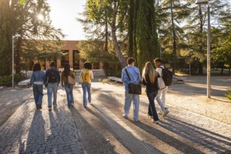 Young diverse students with backpacks walking together along a paved path, heading towards a