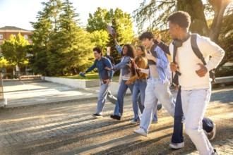 Group of diverse university students with backpacks running across campus at golden hour, laughing