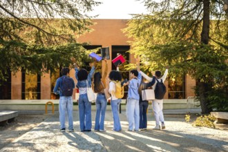 Diverse students seen from behind on a sunlit campus path throwing colorful notebooks into the air