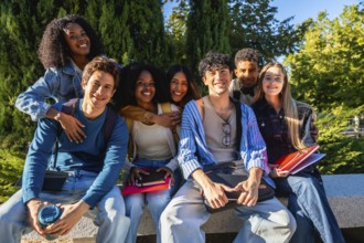 Diverse group of happy young male and female university students sitting outdoors on campus,