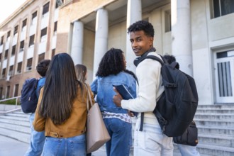 Group of diverse young university students with backpacks and books walking up the steps towards a