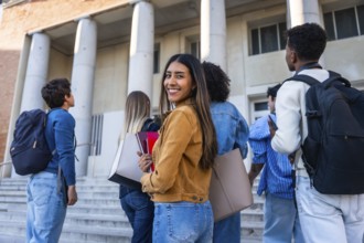 Group of young diverse students walking up steps towards a university building, carrying backpacks