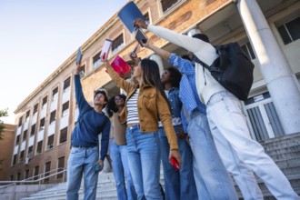 Group of happy young university students raising books and smartphones in the air, celebrating