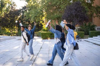 Diverse group of young university students walking on campus after classes, happily raising arms in
