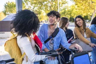 Young diverse students laughing and chatting with bikes and books on a sunny university campus,