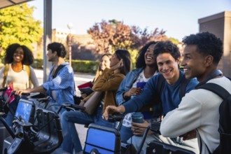 Group of smiling diverse university students standing at a bike sharing station on campus,