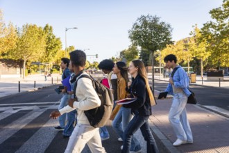 Group of diverse university students with backpacks and books walking across a pedestrian