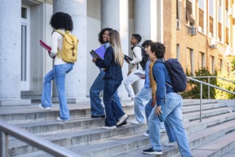 Diverse group of college students walking up campus stairs with backpacks and books, enjoying sunny