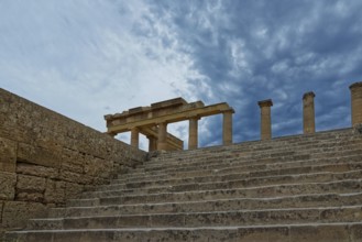 Ancient ruins with stone steps and columns of the Acropolis of Lindos under a dramatic sky,