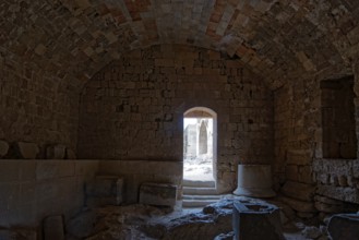 Dark room in ancient stone ruin with vault and doorway leading into the light, Acropolis, Lindos,