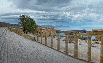Ancient columns and staircase of the Acropolis of Lindos with a view of the sea and cloudy sky,