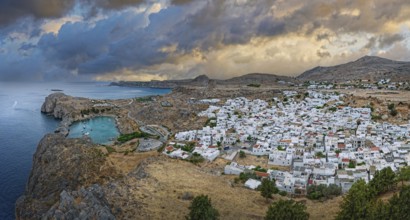 Atmospheric view of the coastal town of Lindos under a dramatic sky at dusk, Acropolis, Lindos,