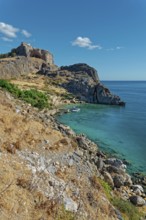 Steep cliffs Paulus Bay of Lindos over crystal clear blue water under a bright blue sky, Acropolis,