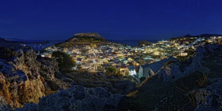 View of the illuminated town of Lindos with the ancient Acropolis under a starry sky with the sea,