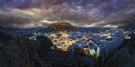 City view of Lindos with the ancient Acropolis at night with dramatic clouds, illuminated buildings