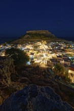Night picture of the brightly lit town of Lindos and the ancient Acropolis on a rock in the