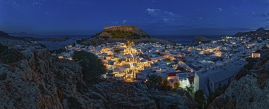 Panorama of picturesque Lindos and the ancient Acropolis at night with illuminated buildings and