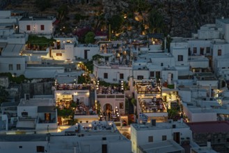 View of the illuminated roof terraces and restaurants of the town of Lindos and white houses that