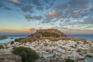 View of picturesque Lindos with the ancient Acropolis on a hill surrounded by the sea at sunset,