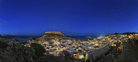 Wide angle photo of the city of Lindos with the ancient Acropolis in a clear night sky with glowing