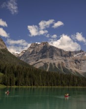 People canoeing on Emerald Lake, bordered by trees and the Canadian Rocky Mountains under a clear
