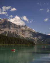 Canoes gliding across Emerald Lake with forested Canadian Rocky Mountains and a clear sky backdrop