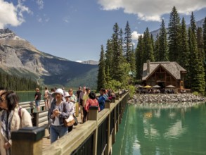 Tourists walking on a wooden bridge over Emerald Lake leading to a cabin, part of Emerald Lake